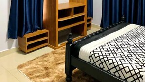 A bedroom with a bed, a wooden wardrobe with shelves, and blue curtains. - Silver Stone Cribs (Kampala)