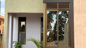 A modern two-story building with a flat roof, a large window on the second floor, and a small potted plant on the ground floor. - Silver Stone Cribs (Kampala)