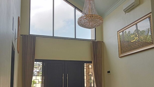 A spacious living room with a large window, a chandelier, a sofa, and a coffee table. - EXPRESS O 91708 Rumah Sriwijaya 12a Syariah (Jember)