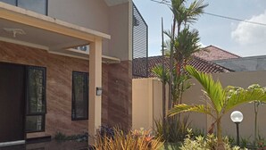 A modern house with a covered patio, a tiled driveway, and a garden with various plants and a street lamp. - EXPRESS O 91708 Rumah Sriwijaya 12a Syariah (Jember)