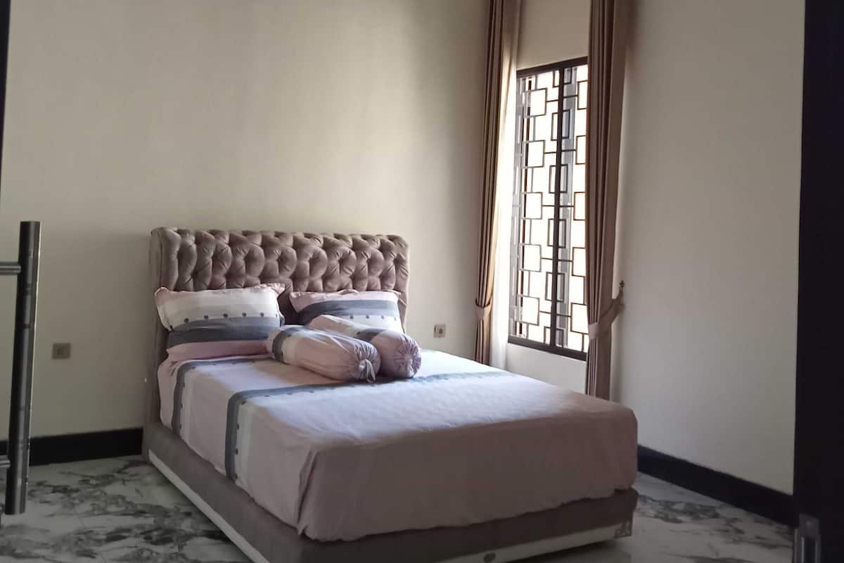 A bedroom with a bed, a ceiling fan, an air conditioning unit, a window with curtains, and a marble floor.