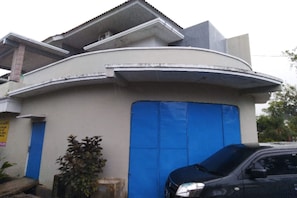 Un edificio con puerta azul, un coche aparcado y una planta cerca de la entrada.