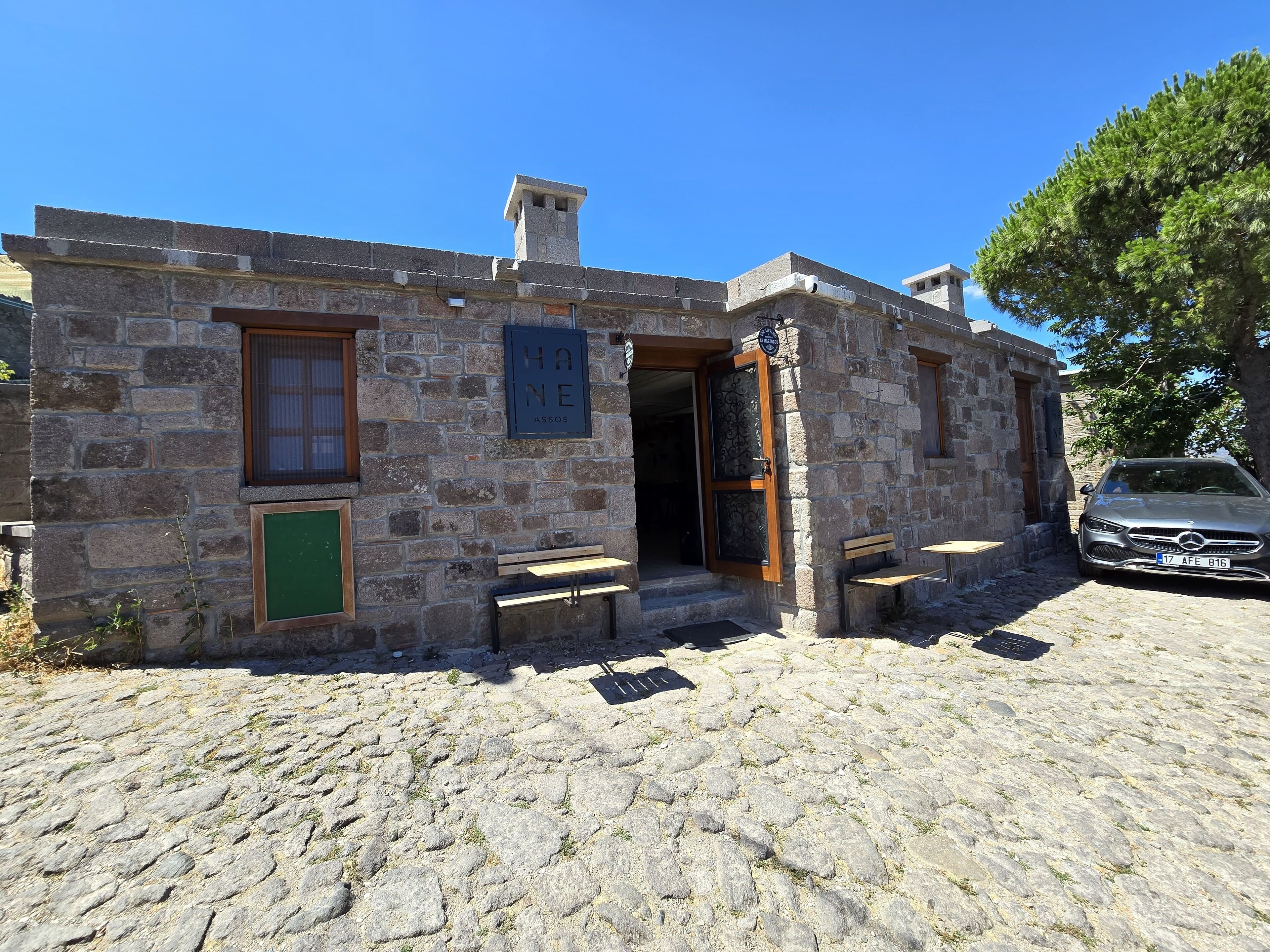 A stone building with a wooden door, a bench outside, and a car parked nearby.
