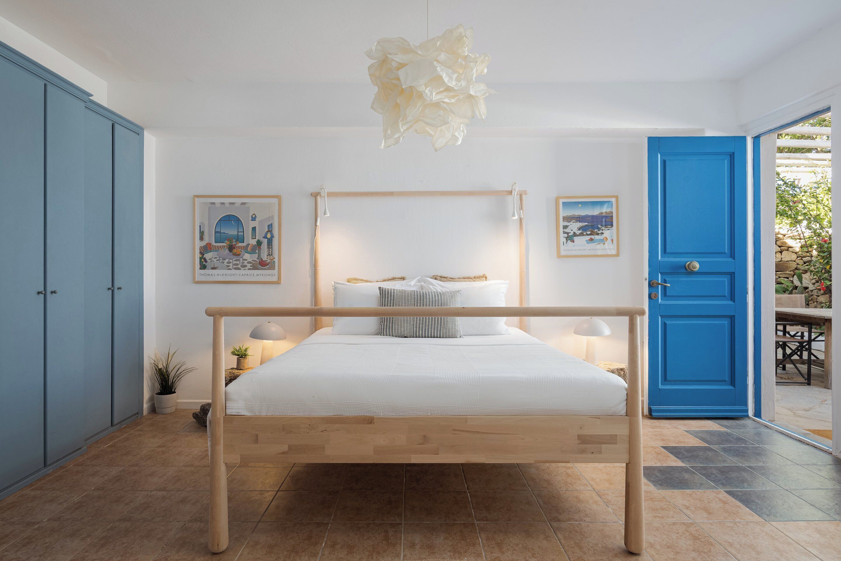 Ein Schlafzimmer mit einem hölzernen Bett, weißer Bettwäsche, einer blauen Tür und zwei gerahmten Bildern an der Wand.