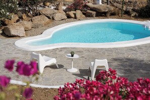 A swimming pool with white chairs and a small table, surrounded by rocks and flowers. - Bougainvillea Comfort Villa Mykonos (Mykonos)