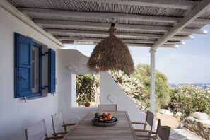 A table with a fruit bowl, white walls, blue shutters, and a view of the sea. - Bougainvillea Comfort Villa Mykonos (Mykonos)