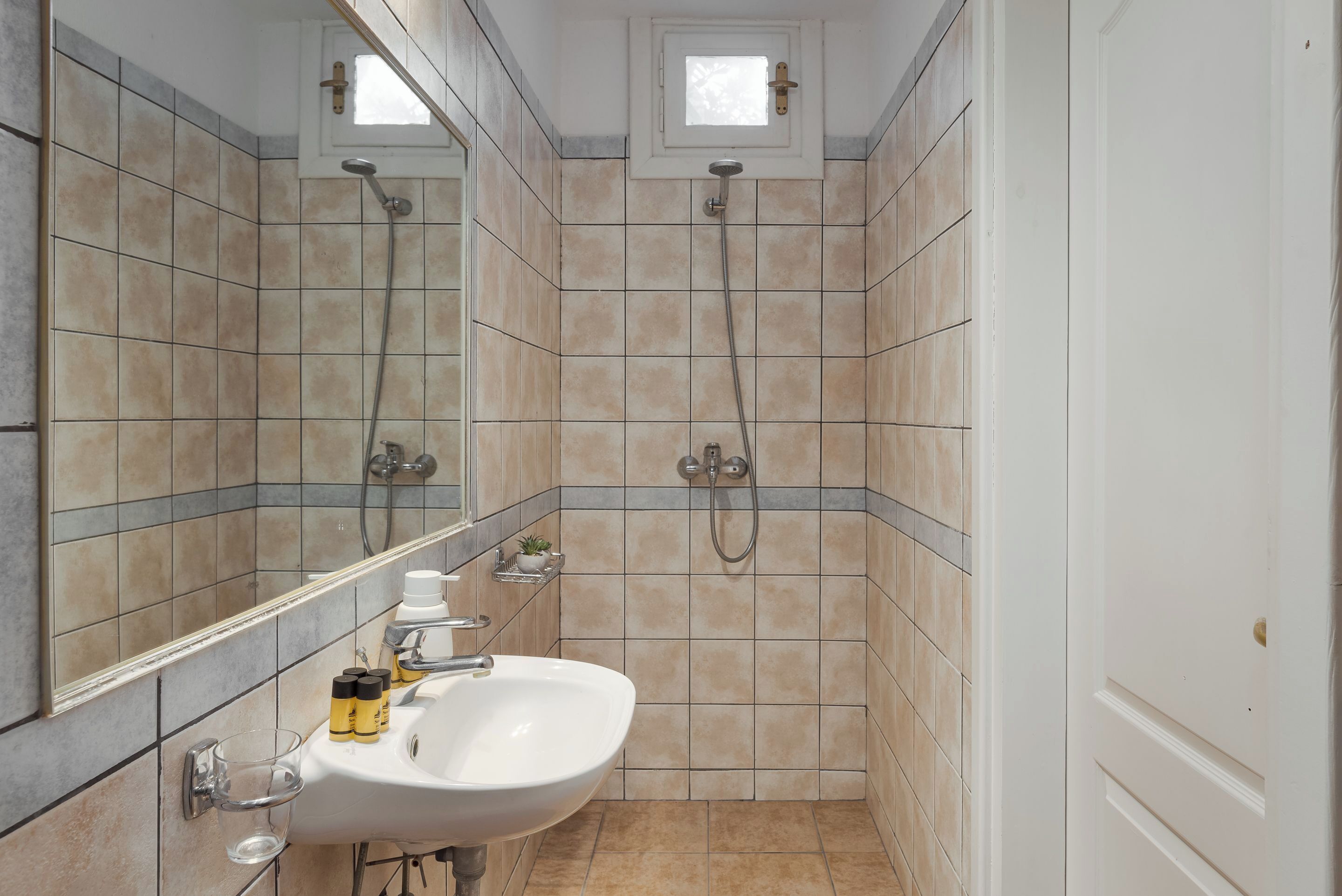 A bathroom with a sink, mirror, shower, and tiled walls.