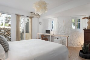 A bedroom with a large bed, a desk, and a stone wall. - Bougainvillea Comfort Villa Mykonos (Mykonos)