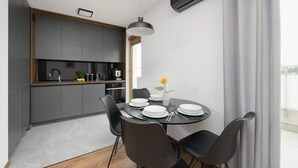 A modern kitchen with dark cabinetry, a round dining table with black chairs, and a pendant light. - Modern Apartment | Private Parking and Balcony (Konstancin-Jeziorna)