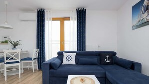 A living room with a dark blue sofa, a white coffee table, and a dining area with white chairs and a table. - Charming Apartment near Warsaw | Parking, Air Conditioning (Konstancin-Jeziorna)
