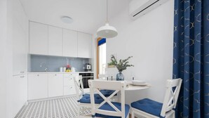 A compact kitchen with white cabinets, a dining area with two white chairs and a round table, and a blue curtain on the right. - Charming Apartment near Warsaw | Parking, Air Conditioning (Konstancin-Jeziorna)