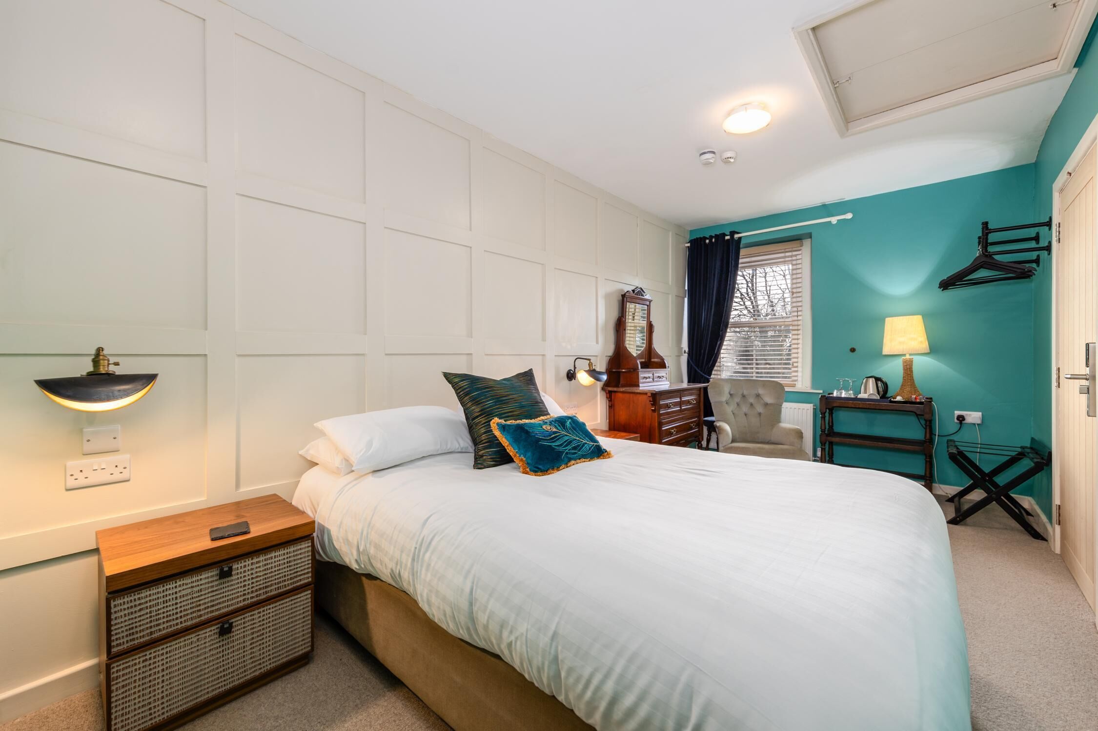 Une chambre à coucher comprenant un lit, une table de chevet, une lampe, une horloge et une fenêtre avec des rideaux.