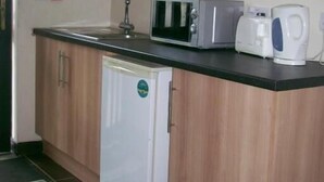 A compact kitchen with a microwave, toaster, and coffee maker on the counter, a refrigerator, and a sink. - The Red Admiral Hotel (Seascale)