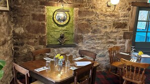 A dining area with a stone wall, a mirror, and a table set for four with chairs. - The Red Admiral Hotel (Seascale)