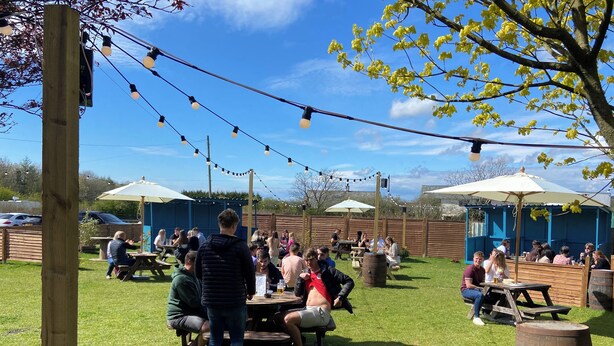 An outdoor seating area with tables and umbrellas, surrounded by a wooden fence and trees. - The Red Admiral Hotel (Seascale)