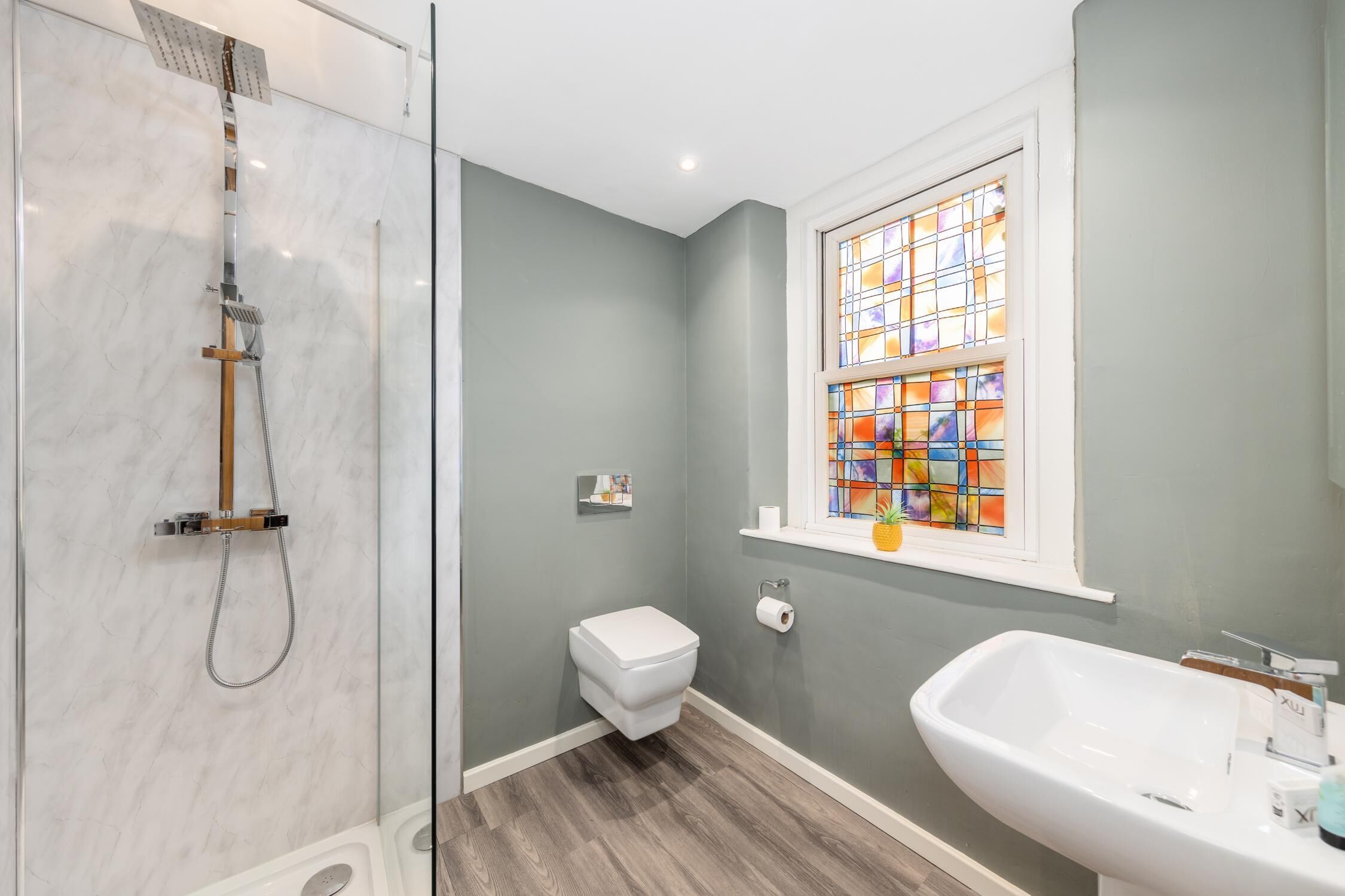 A bathroom with a glass shower enclosure, a toilet, a sink, and a stained glass window.
