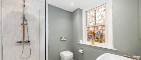 A bathroom with a glass shower enclosure, a toilet, a sink, and a stained glass window.