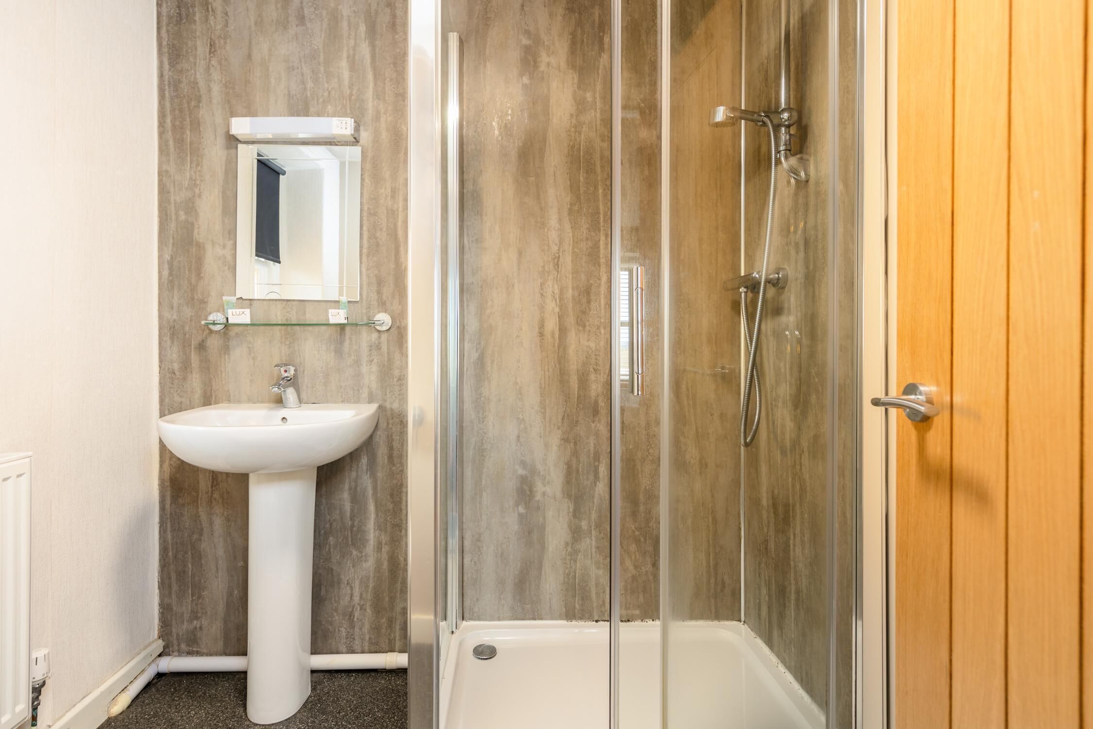 A bathroom with a pedestal sink, a glass-enclosed shower, and a wooden door.