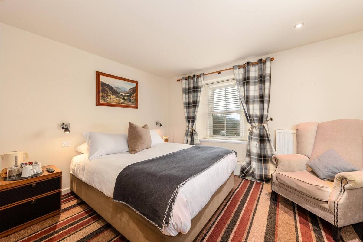A bedroom with a bed, a chair, a nightstand, a window with curtains, and a painting on the wall.