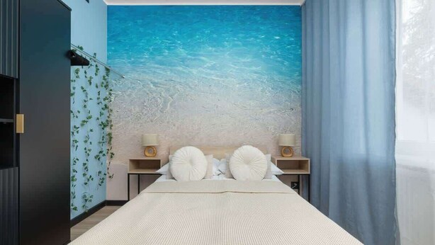 A bedroom with a large bed, a nightstand with a lamp, and a wall mural of a beach scene.