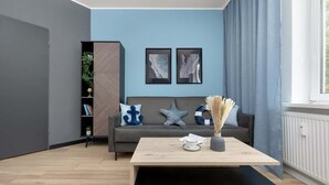 A modern living room with a grey sofa, two framed artworks, a wooden coffee table, and a window with curtains.