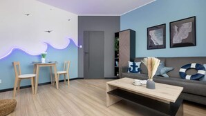 A modern living room with a wooden coffee table, two wooden chairs, a grey sofa with nautical-themed cushions, and wall art depicting maps.
