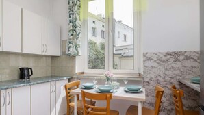Eine Küche mit weißen Schränken, einer Marmor-Spritzschutzwand und einem Esstisch, gedeckt für vier Personen, mit blauen Tellern und einem Blumenstrauß.