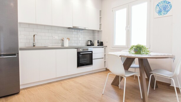 Une cuisine moderne avec des armoires blanches, un réfrigérateur en acier inoxydable, un four encastré et un coin repas comprenant une table ronde et des chaises blanches.
