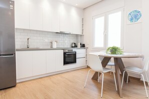 Une cuisine moderne avec des armoires blanches, un réfrigérateur en acier inoxydable, un four encastré et un coin repas comprenant une table ronde et des chaises blanches.