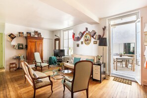 A spacious living room with a wooden floor, a television, a sofa, and a dining area with a table and chairs.