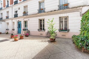 A courtyard with potted plants, a blue door, and a building with multiple windows and balconies.