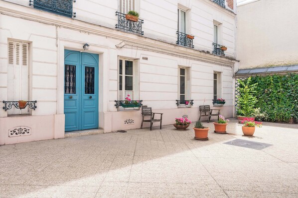 Un edificio con puerta azul, plantas en macetas y un patio empedrado.