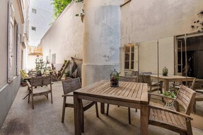 Un patio al aire libre con mesas y sillas de madera, plantas en macetas y un column grande.