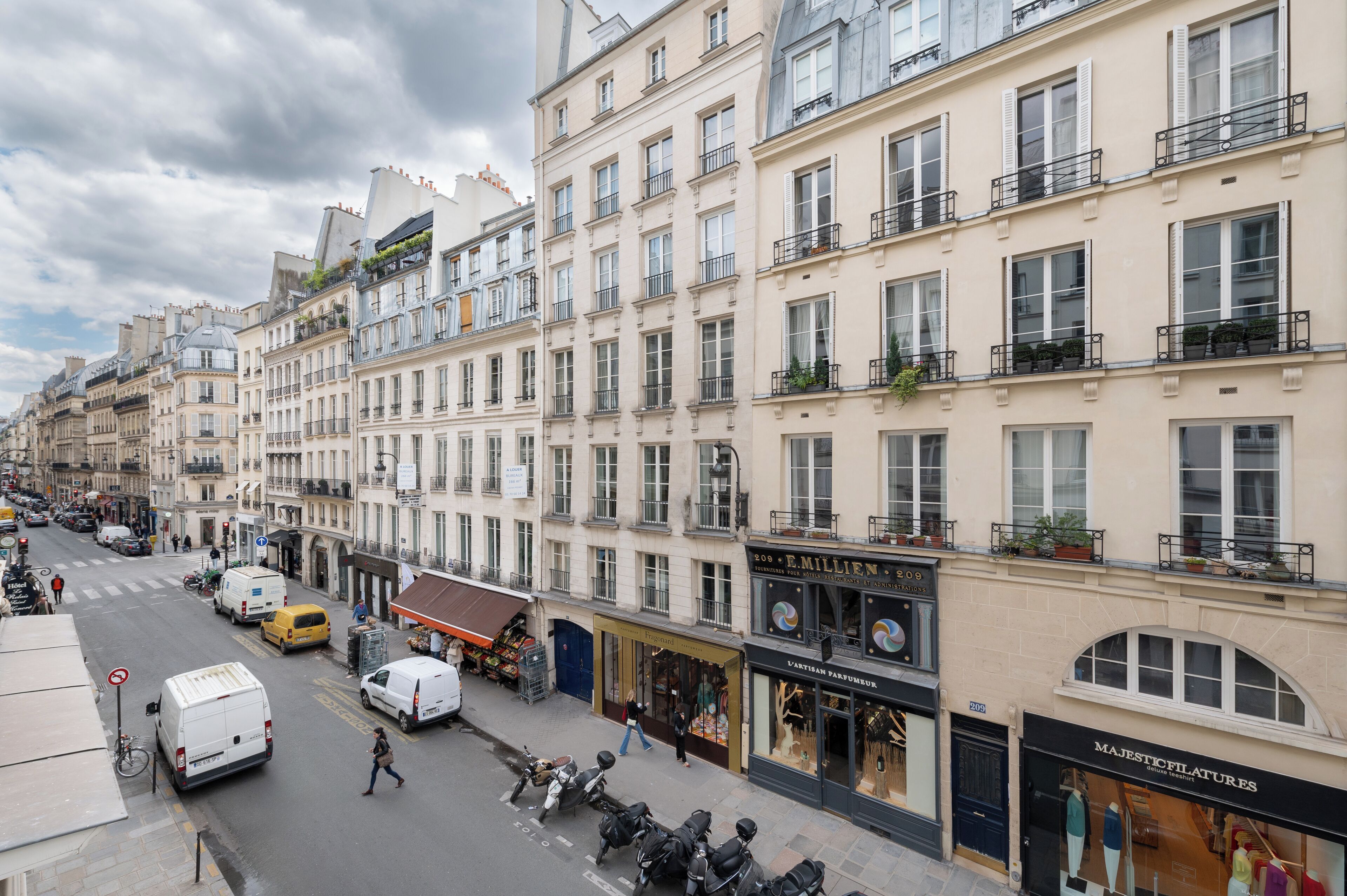 A street view of Parisian buildings with shops and a white van parked on the side.