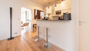 Une cuisine moderne dotée d’appareils électroménagers en acier inoxydable, d’un plancher en bois et de deux tabourets de bar.