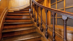 Un escalier en bois, doté de balustres décorées et d’une rambarde en verre.