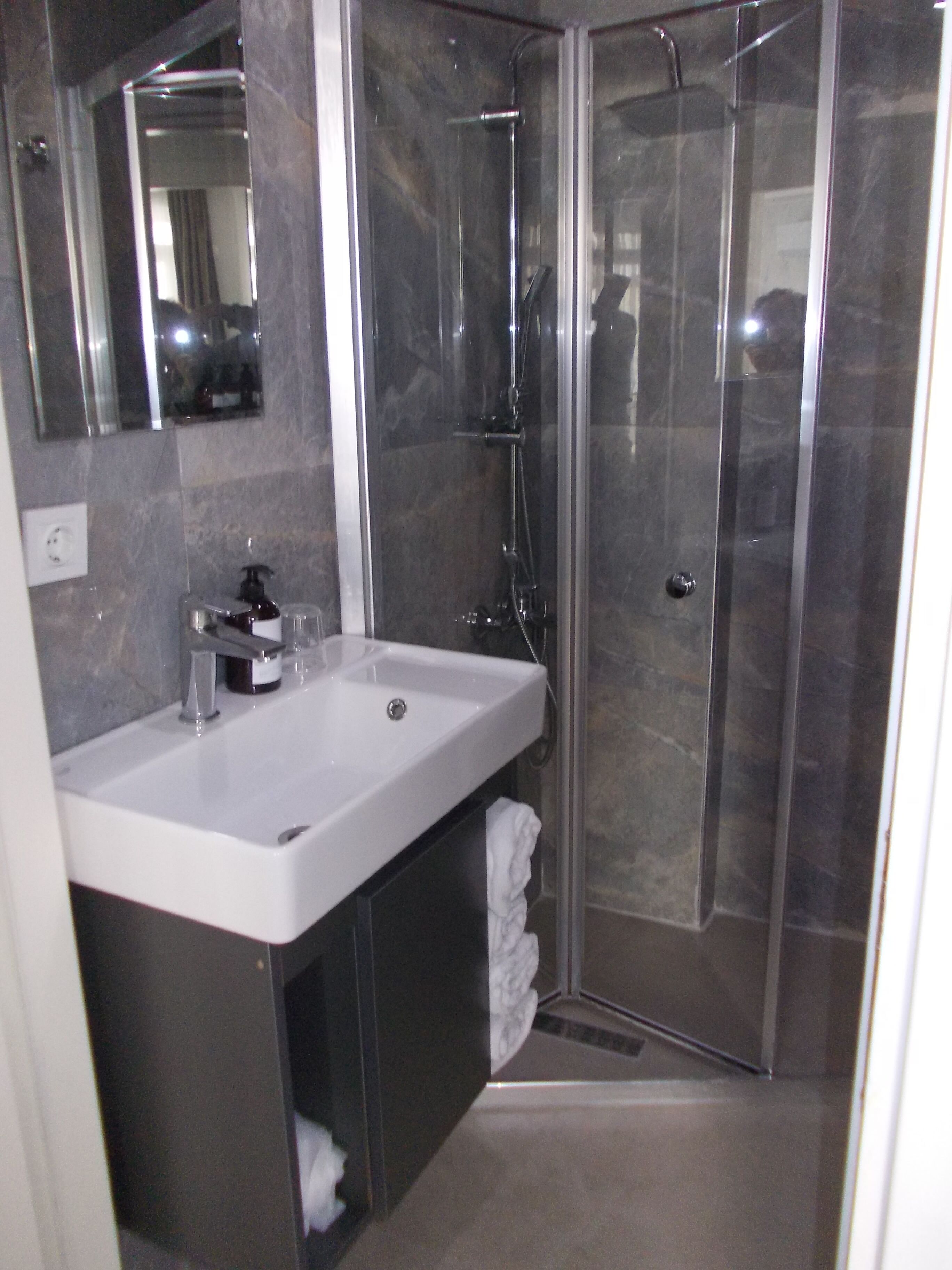 A modern bathroom with a large mirror, a white sink, a glass shower enclosure, and a towel rack.