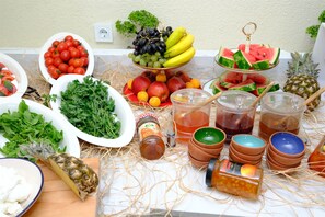 A table with various fruits, vegetables, and drinks, including tomatoes, grapes, bananas, apples, and a pineapple. - Sorta Hotel (Konyaalti)