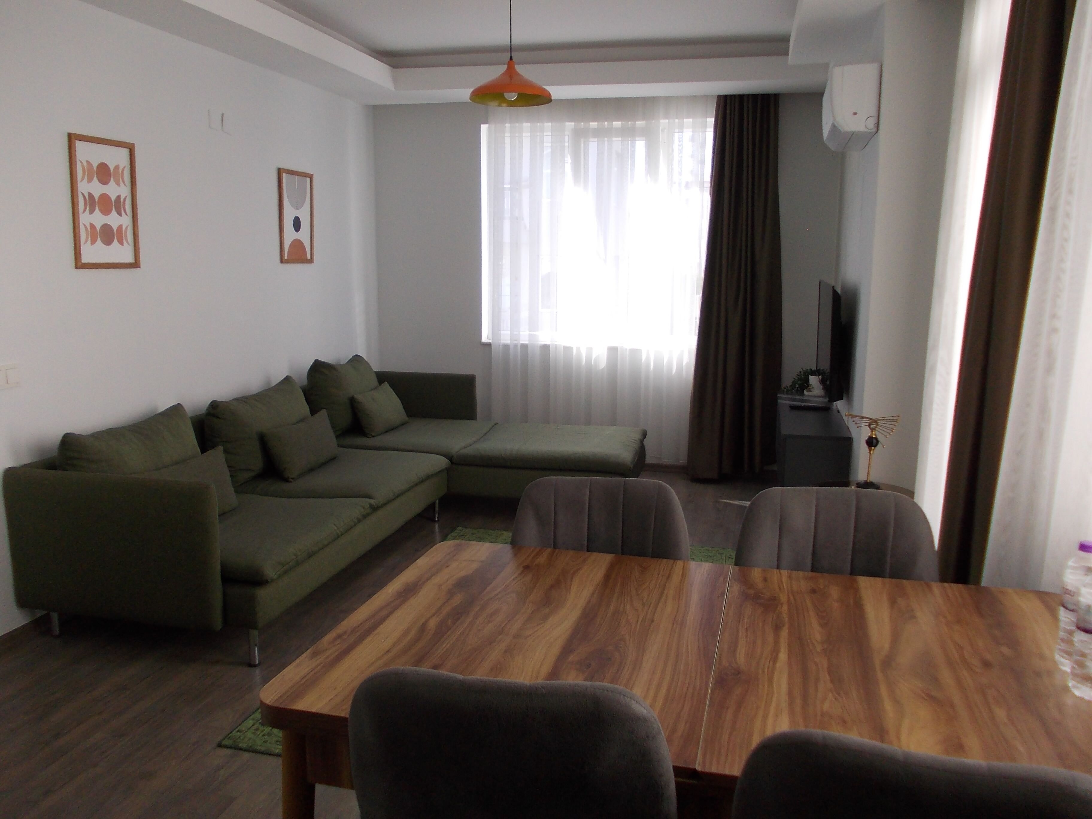A living room with a sectional sofa, a wooden dining table, and a television.