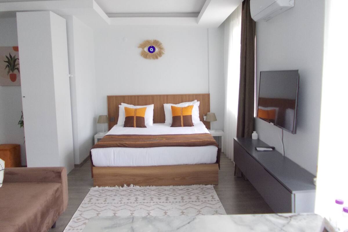 Una habitación de hotel con cama, mesitas de noche, televisión, espejo y puerta.