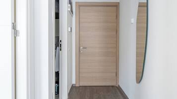 Un pasillo con una puerta de madera, un perchero con toallas y un espejo en la pared.