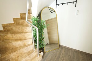 Una escalera con escalones de mármol, una planta en maceta y un espejo grande que refleja una puerta de madera.