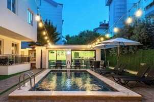 An indoor swimming pool with a bar area, lounge chairs, and string lights.