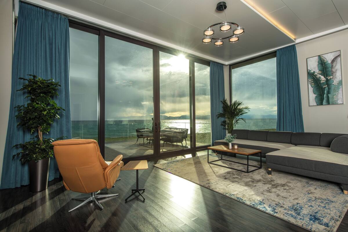 Een moderne woonkamer met een grote glazen deur die uitkomt op een balkon met uitzicht op een waterpartij.