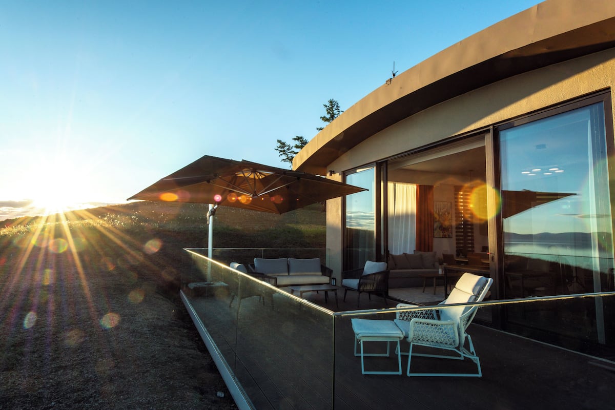Een modern balkon met buitenruimte, voorzien van glazen balustrades, een zithoek met stoelen en een bank, en een grote parasol voor schaduw.