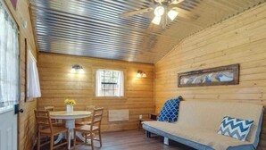 L’intérieur d’un chalet en bois comprend une table à manger, des chaises, un canapé, un ventilateur de plafond et deux fenêtres.