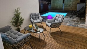 Un patio con piscina, piso de madera y mobiliario.