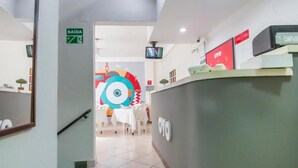 Zona de recepción con mostrador, señalización de salida y un mural de colores al fondo.