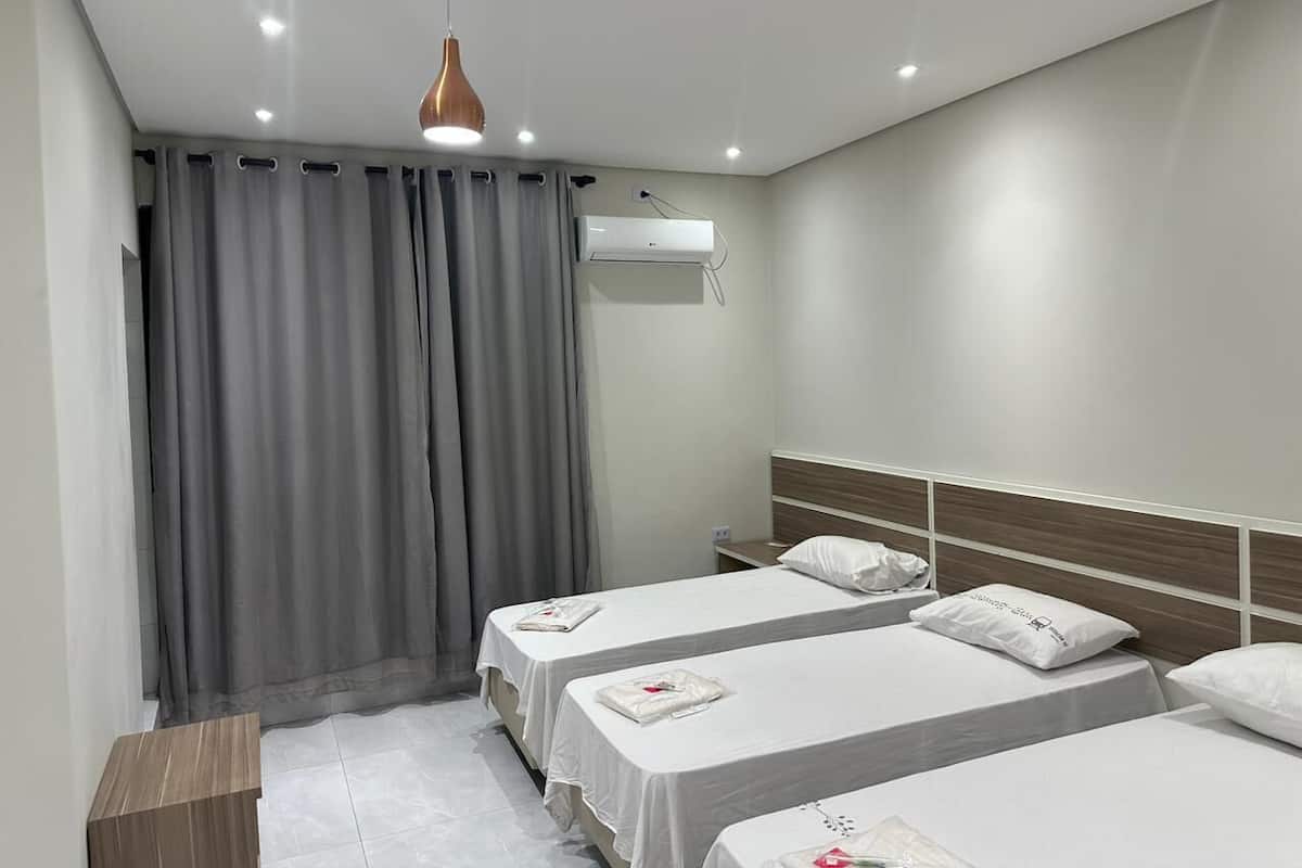 Une chambre d’hôtel avec deux lits simples, une table de chevet en bois, un climatiseur fixé au mur et une lampe suspendue.