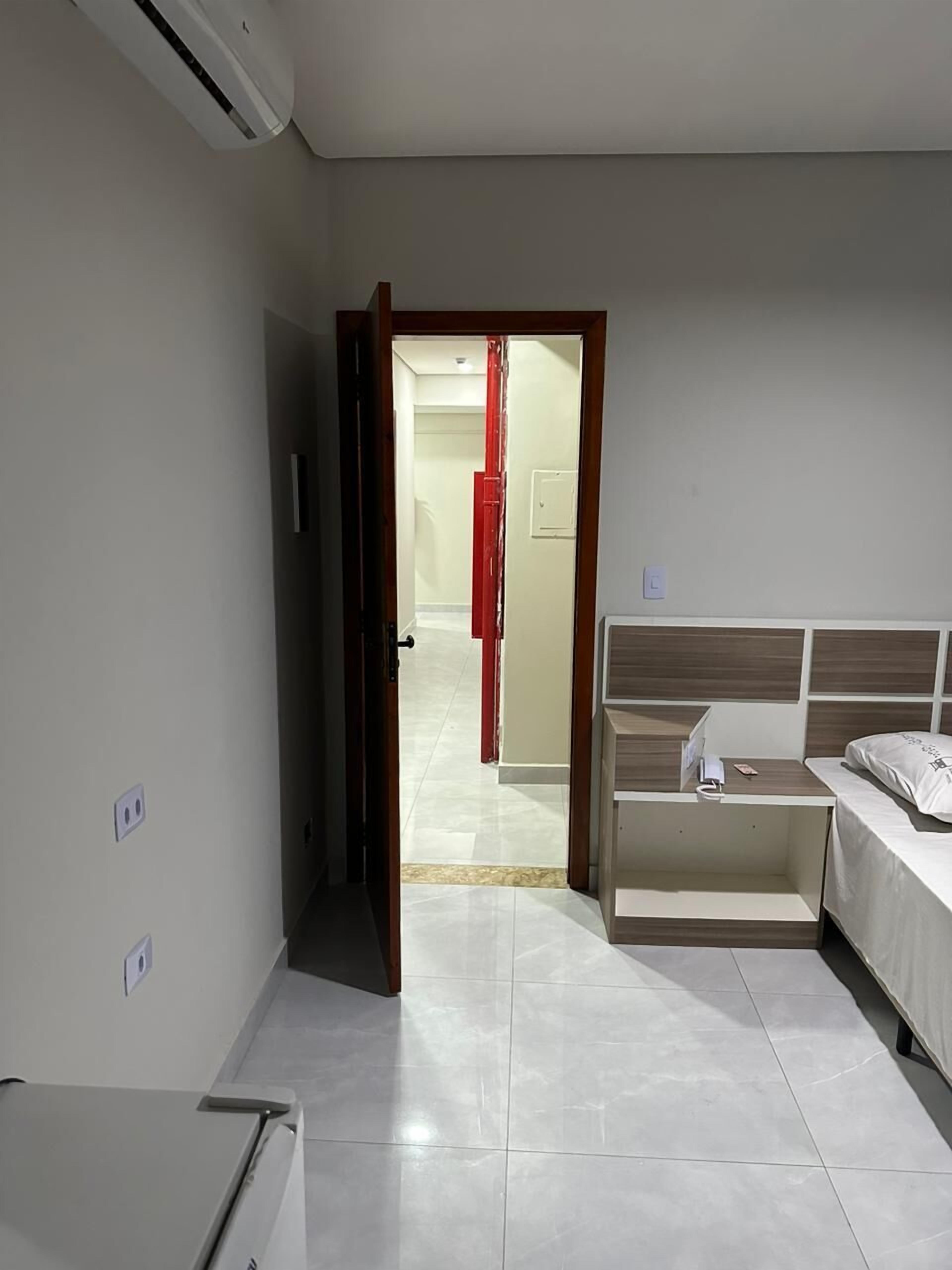 Une chambre d’hôtel avec un lit, un bureau et une armoire. Une porte donne accès à une autre pièce.